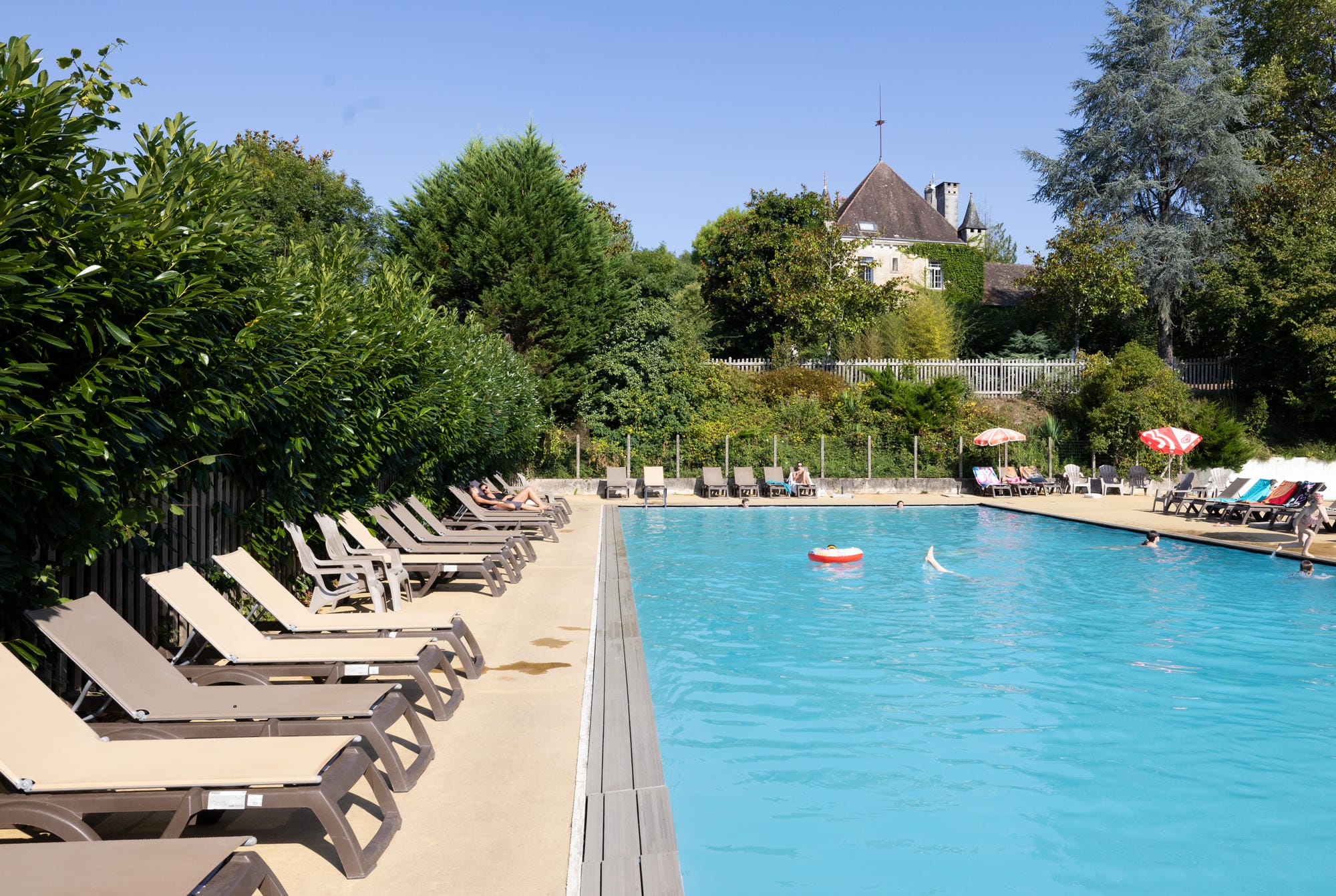 Piscine extérieure avec transats et vue sur le Château le Verdoyer en Dordogne